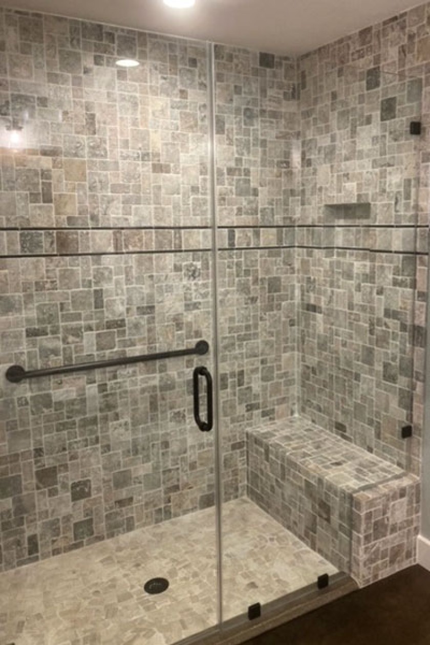 A shower interior with grey and brown tile work.