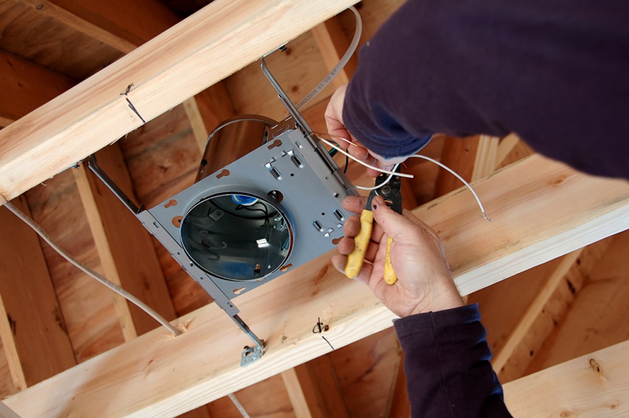 Individual installing an electrical item into the framing of a house.